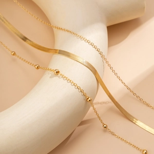 Close-up of golden minimalist snake chain set with bead accents on art sculpture