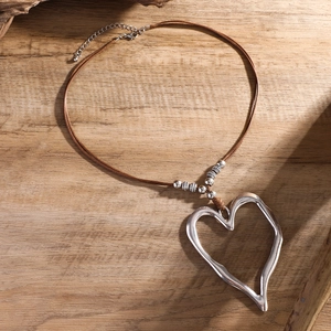 Dettaglio di un grande ciondolo a cuore su cordino cerato marrone con perle di metallo