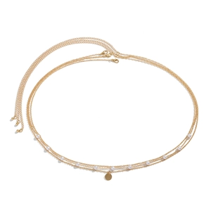 Detail of a layered gold body chain with elegant white pearls and a round charm