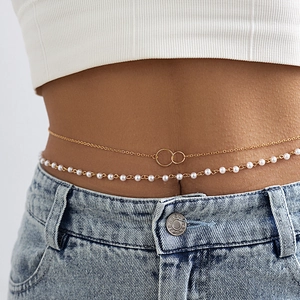 Detailaufnahme der zweilagigen Goldkette und weißen Perlen-Körperkette auf Jeans