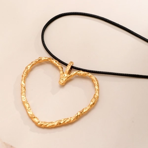 Dettaglio macro del ciondolo a cuore dorato con texture lava su collana cordino nero