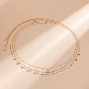 Detail der mehrlagigen goldenen Körperkette mit weißen Perlen, Schmetterlingsanhängern und Verschluss