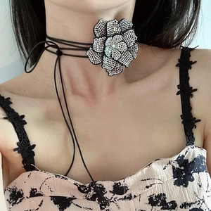 Detail van een bloemenchoker met witte strassteentjes en zwart koord op een model