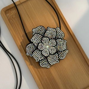 Detail van cameliabloem hanger ketting met regenboog steentjes op houten dienblad