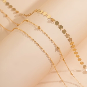 Détail de trois chaînes dorées superposées avec paillettes et perles métalliques