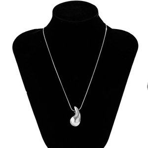 Macro shot of polished silver comma pendant on a sleek snake chain over black velvet