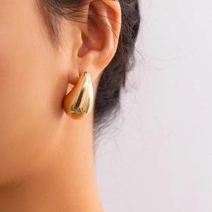 Close-up of a model wearing large polished gold teardrop earrings with a mirror finish