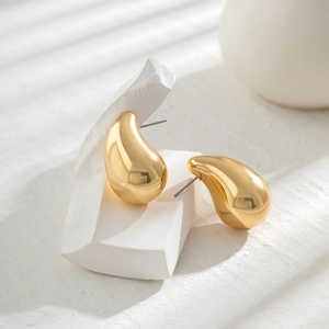 Macro view of minimalist polished gold teardrop earrings on a white stone base