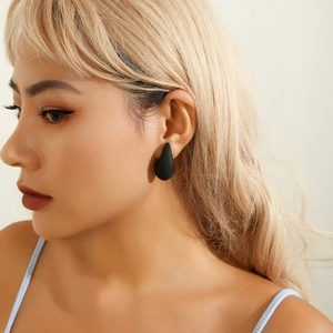 Close-up of a model wearing minimalist matte black teardrop earrings for a modern party look