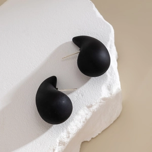 Close-up of minimalist black comma-shaped teardrop earrings on a white stone base