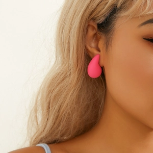 Close-up of matte hot pink teardrop earrings on model with minimalist punk style