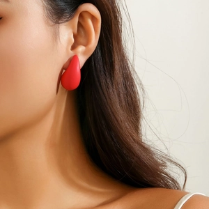 Close-up of a matte red teardrop earring worn by a model in a minimalist portrait