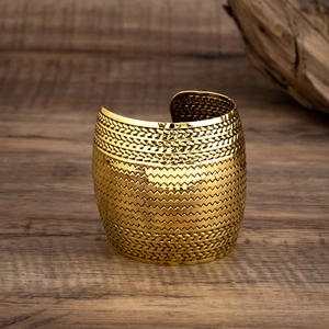 Primer plano de un brazalete punk dorado con texturas grabadas y forma de tambor