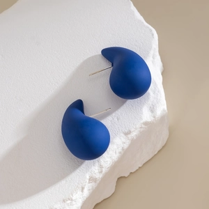 Close-up of matte Klein blue teardrop earrings on a textured stone display