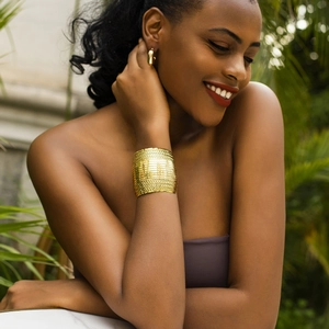 Conjunto de brazalete dorado con textura de malla y pendientes de aro en una modelo