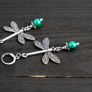 Close-up of vintage dragonfly drop earrings with silver hollow patterns and green beads