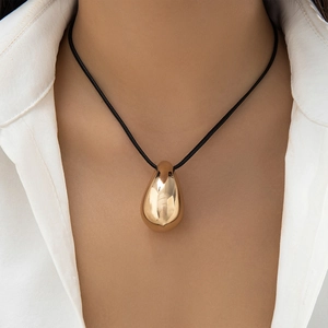 Macro view of a large polished gold teardrop pendant necklace worn over a white shirt