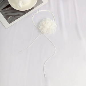 Detailed view of a white fabric flower choker with adjustable thin straps on white cloth