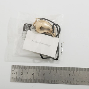 Detail shot of large gold teardrop pendant on black cord next to a measuring ruler
