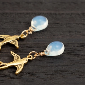 Macro detail of bird earring with opal stone bead and intricate gold wire wrap craft
