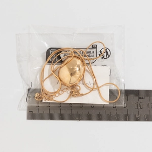 Detailed view of large gold teardrop pendant necklace next to a ruler for size reference