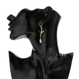 Detail of a gold swallow earring with a blue teardrop stone on a black jewelry bust