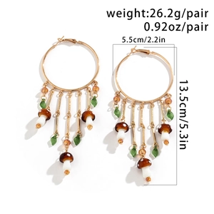 Detailed view of large gold hoop earrings featuring mushroom and leaf tassel pendants