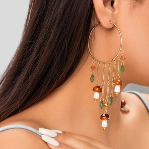 Détail de créoles dorées avec pendentifs champignon et feuilles sur un mannequin