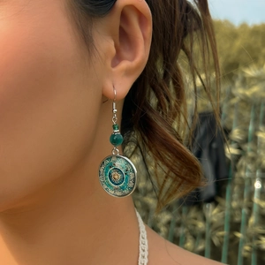 Detail of vintage bohemian dangle earring with green bead and mandala charm on model