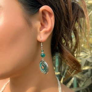 Close-up of ethnic drop earrings with green bead and mandala charm on a model's ear