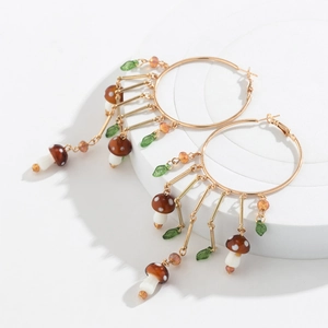Détails de créoles dorées avec pendentifs champignons, feuilles vertes et pampilles