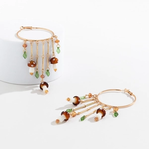 Detail of gold hoop earrings with brown mushroom pendants and green leaf glass beads