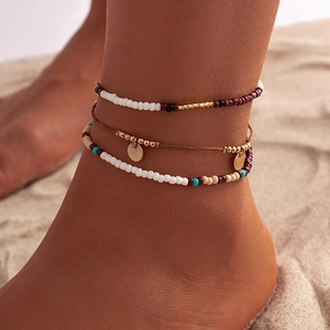 Nahaufnahme von Boho-Perlen-Fußkettchen mit goldenen Anhängern am Sandstrand
