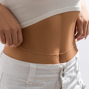 Detailed close-up of a minimalist gold waist chain with delicate beads on a female model
