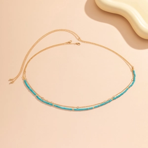 Détail de la chaîne de corps double en or avec perles turquoise et petits cristaux brillants