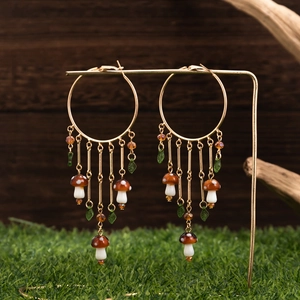 Golden hoop earrings with mushroom tassels and green leaf charms on a forest background