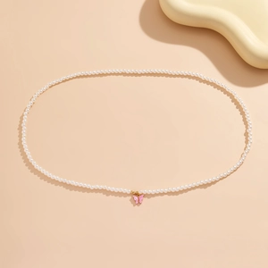 Detail of white faux pearl waist chain featuring a delicate pink butterfly pendant
