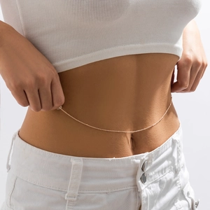 Close-up of minimalist gold beaded belly chain on white denim shorts and rib tank top