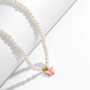Macro detail of elegant pink butterfly pendant with pearls and golden chain metal accents