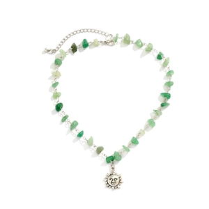 Detail of beaded necklace with green gravel stones and silver sun charm on white background