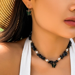 Dettaglio della collana di pietre nere e perle con ciondolo a farfalla verde su modella