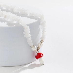 Close-up of beaded necklace with white irregular stones and a red mushroom charm