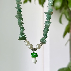 Detail of green stone necklace featuring pearl accents and a mushroom pendant charm