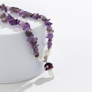 Macro shot of purple gravel necklace with white pearls and polka dot mushroom pendant