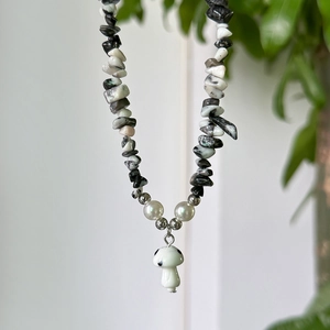 Detail of beaded necklace featuring irregular black and white stones and mushroom charm