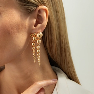 Gros plan sur des boucles d'oreilles pompons dorées avec sphères métalliques