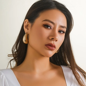 Close-up of large gold teardrop earrings worn by a model in a minimalist modern style