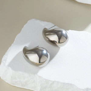 Detailed view of polished silver waterdrop earrings on a textured white stone base