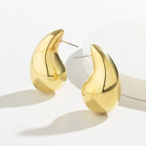 Macro shot of gold teardrop earrings with mirror finish on white cylindrical display