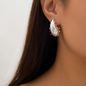 Close-up of a silver comma-shaped drop earring with sparkling crystals on a model